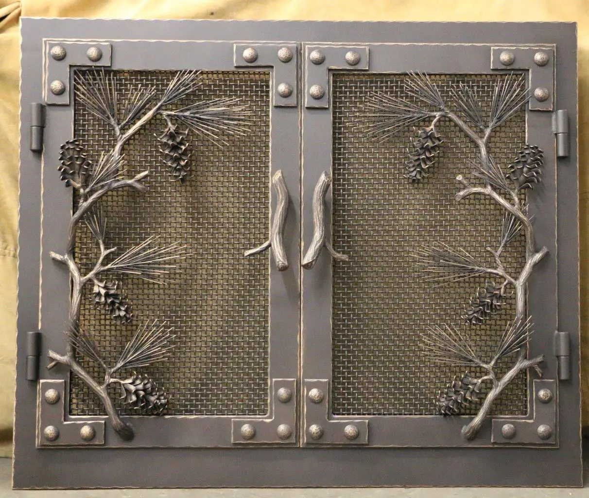 A fireplace screen with metal branches and pine cones.