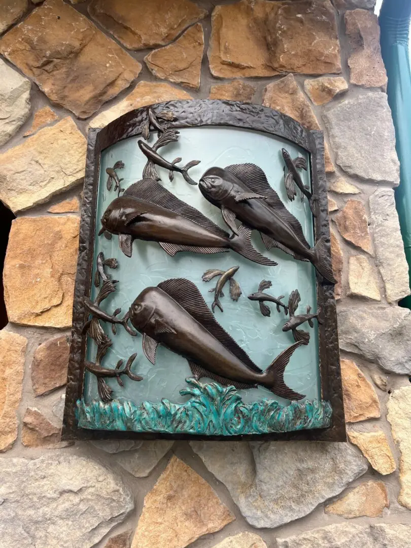 A metal picture of three dolphins on the side of a building.